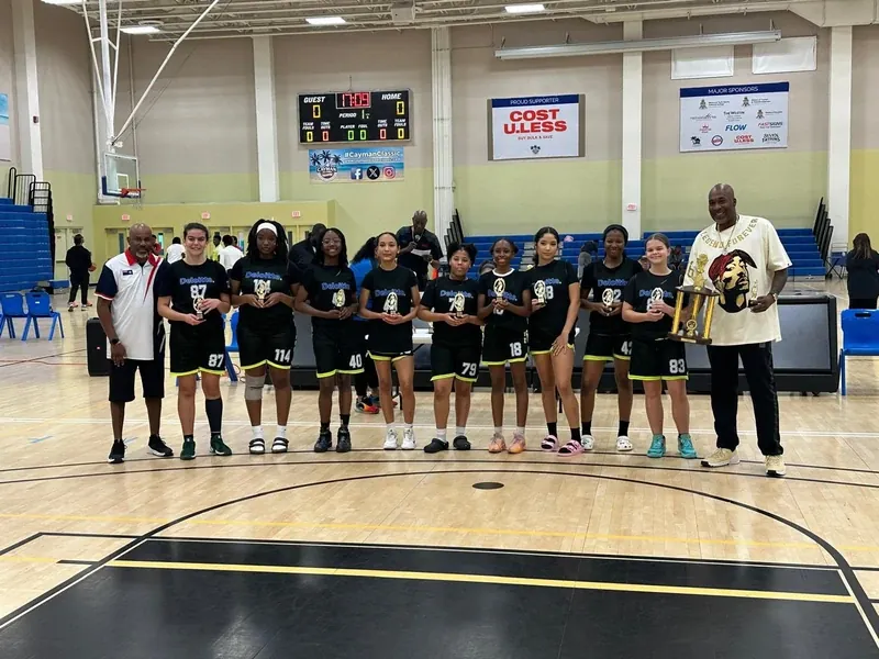 Cayman Islands women's basketball team with coach Cory McGee and a trophy